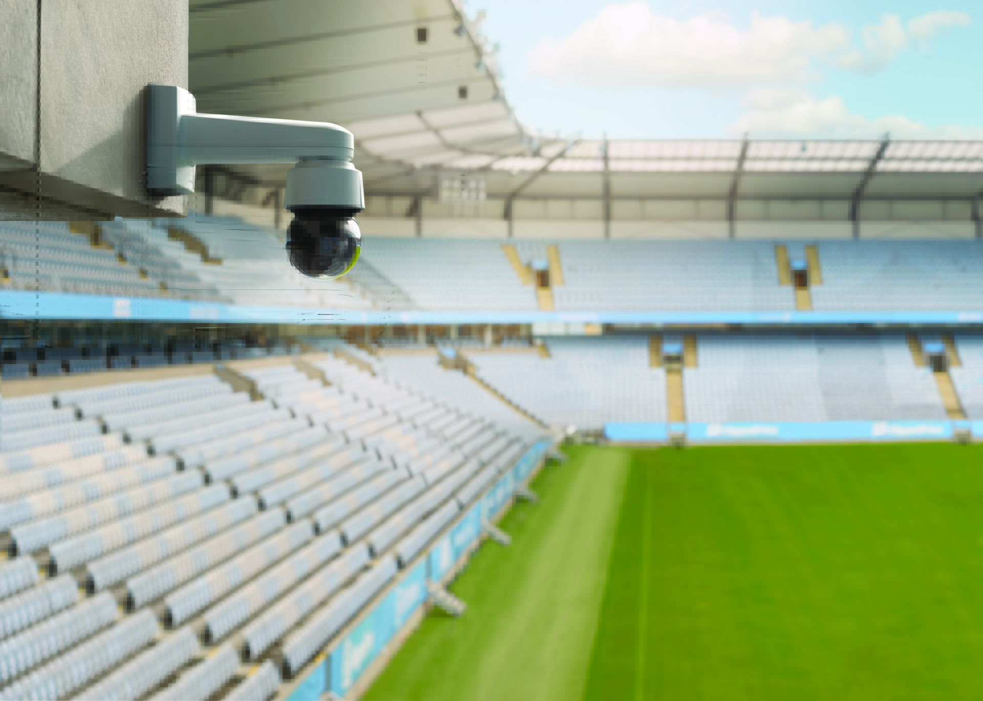 AXIS Q6135-LE PTZ Network Camera installed on a wall mount overlooking a football stadium pitch and seating area.