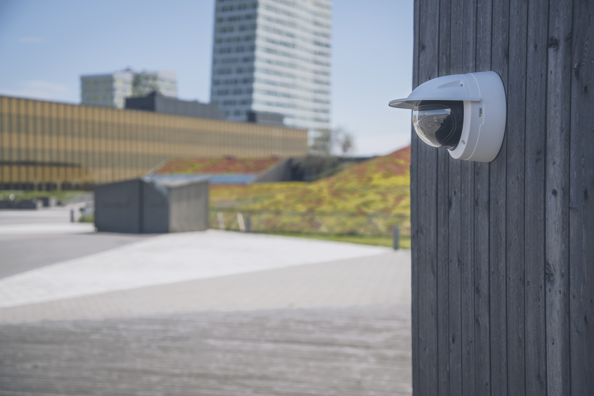 AXIS P3818-PVE panoramic multisensor camera mounted on a wooden wall overlooking a public park.