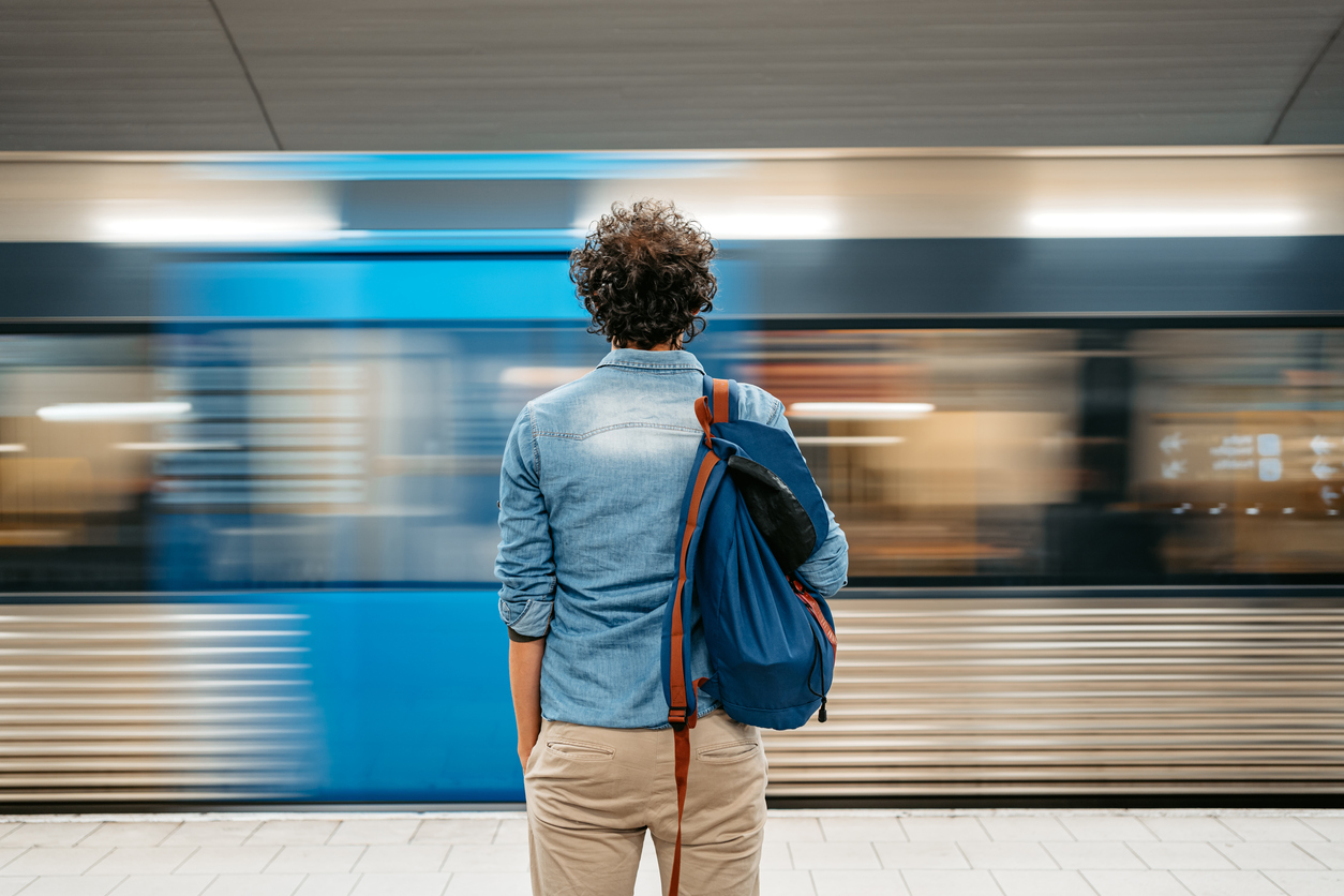 Person with backpack waiting on a metro platform as a train speeds past, symbolising smart city video surveillance on public transport.
