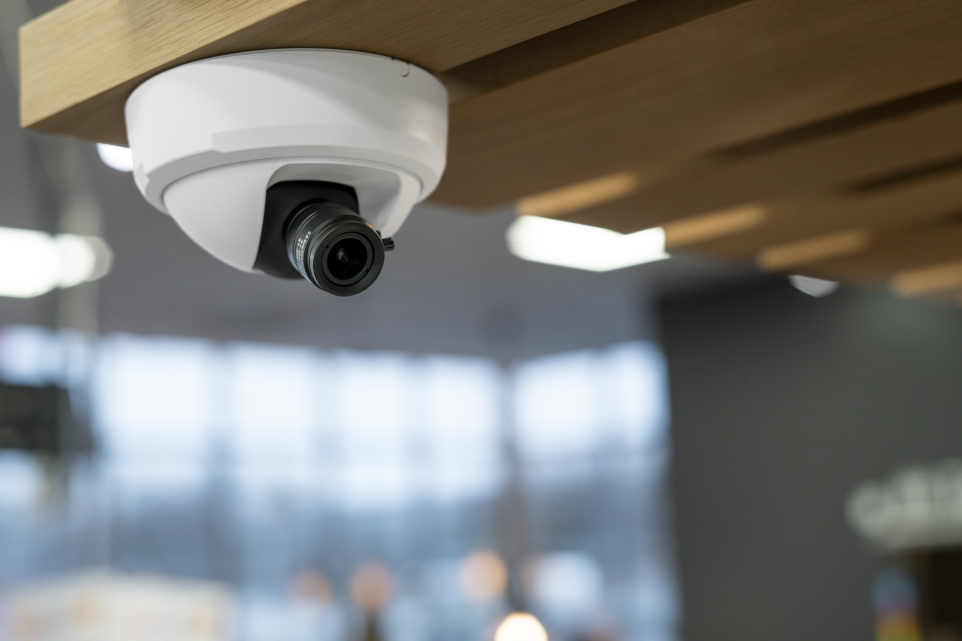 AXIS P1275-Mk II dome camera mounted on a wooden ceiling, with lens directed downward into a modern interior space.