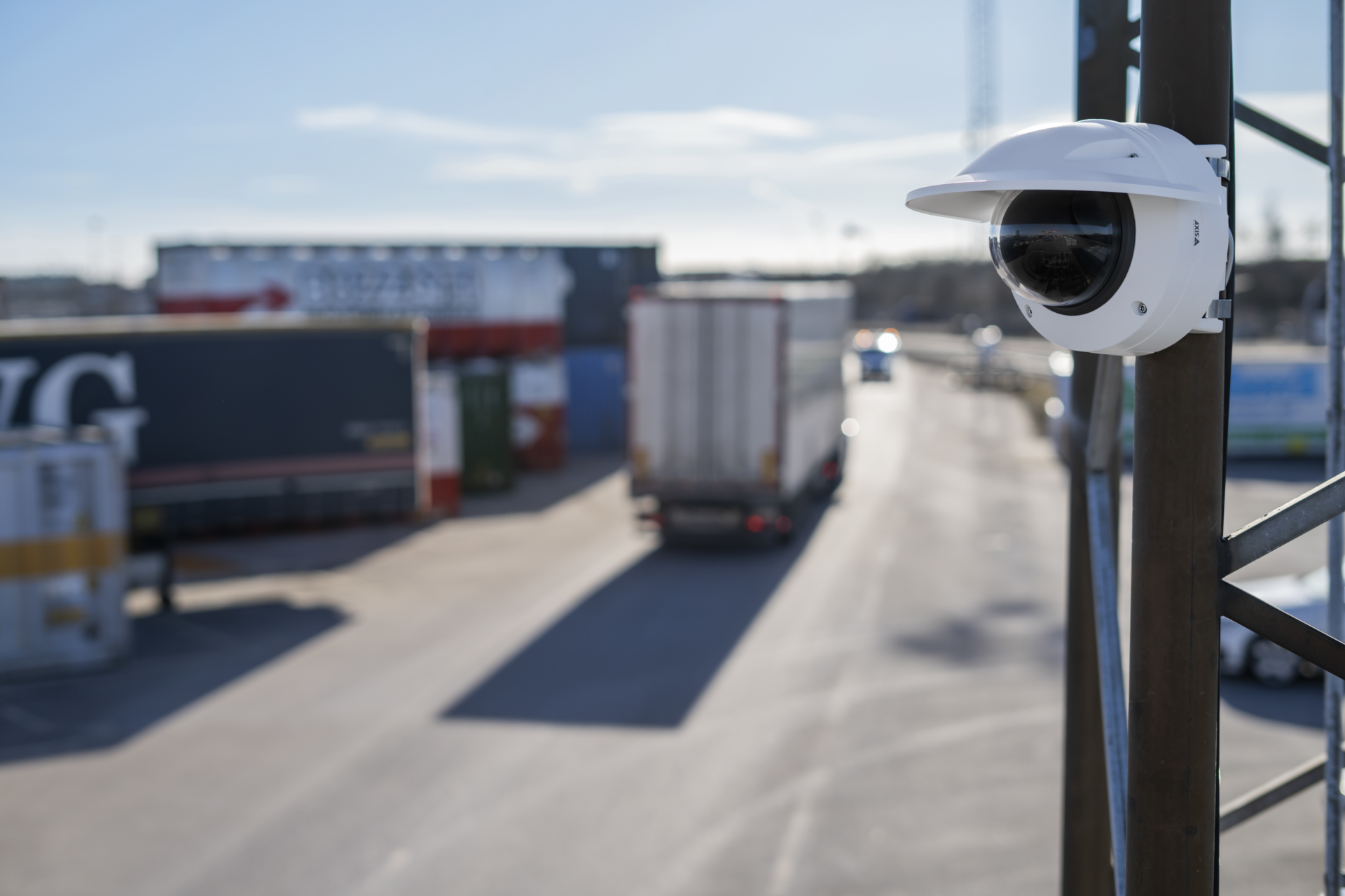 AXIS Q3628-VE dome camera mounted on a pole at a logistics terminal, with trucks and freight containers visible in the background.