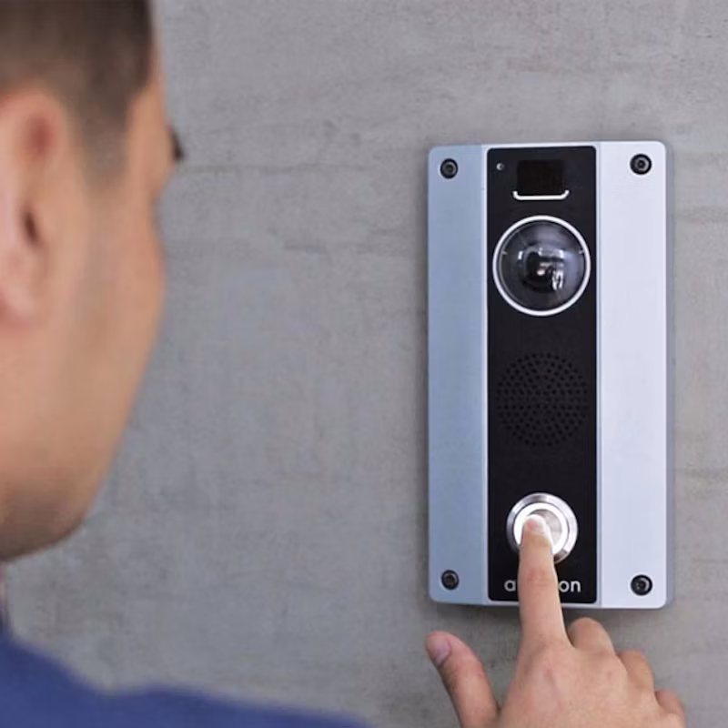 A man pressing the call button on an Avigilon H4 Video Intercom mounted on a concrete wall.
