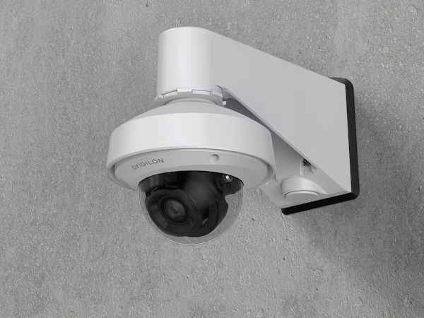 A white Avigilon H6SL dome camera mounted on a textured grey concrete wall using a pendant arm bracket.
