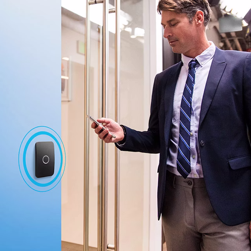 Man using a mobile phone to authenticate entry via an Avigilon Alta Smart Reader at a commercial glass door.