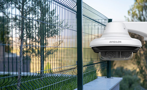Avigilon multi-sensor dome camera mounted on a green metal perimeter fence for wide area surveillance.